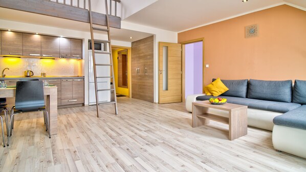 A modern living room with a sofa, a coffee table with fruit, a kitchen area with a microwave, and a wooden floor.