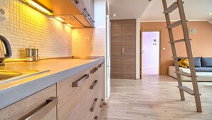 A modern kitchen with a wooden countertop, a stainless steel sink, and a built-in oven. There is a wooden ladder leaning against the wall, and a wooden door leading to another room.