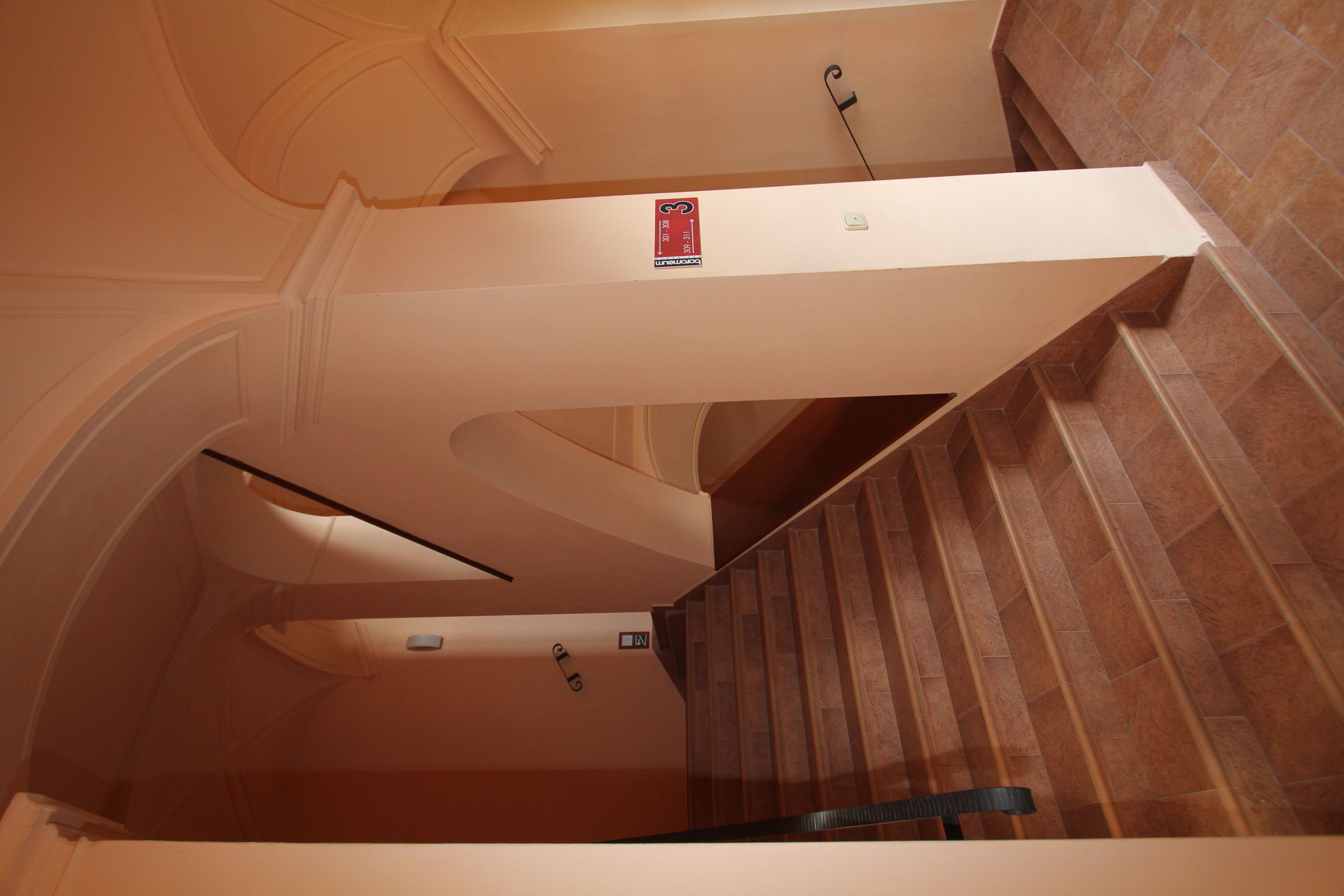A staircase with a handrail, a fire alarm pull station, and a sign indicating the direction to the emergency exit.