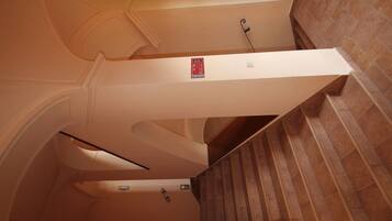 A staircase with a handrail, a fire alarm pull station, and a sign indicating the direction to the emergency exit.