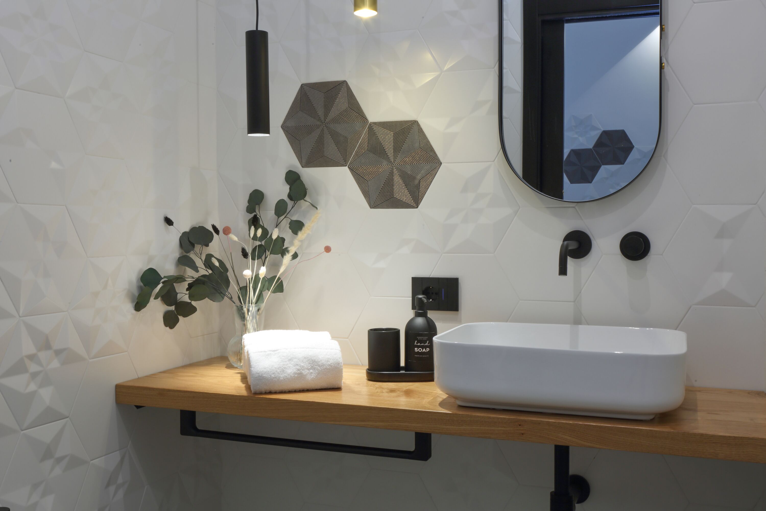A modern bathroom with a wooden vanity, a white sink, a mirror, and geometric wall tiles.