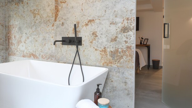 Un baño moderno con una bañera independiente, un grifo empotrado en la pared y una mesita con artículos de aseo.