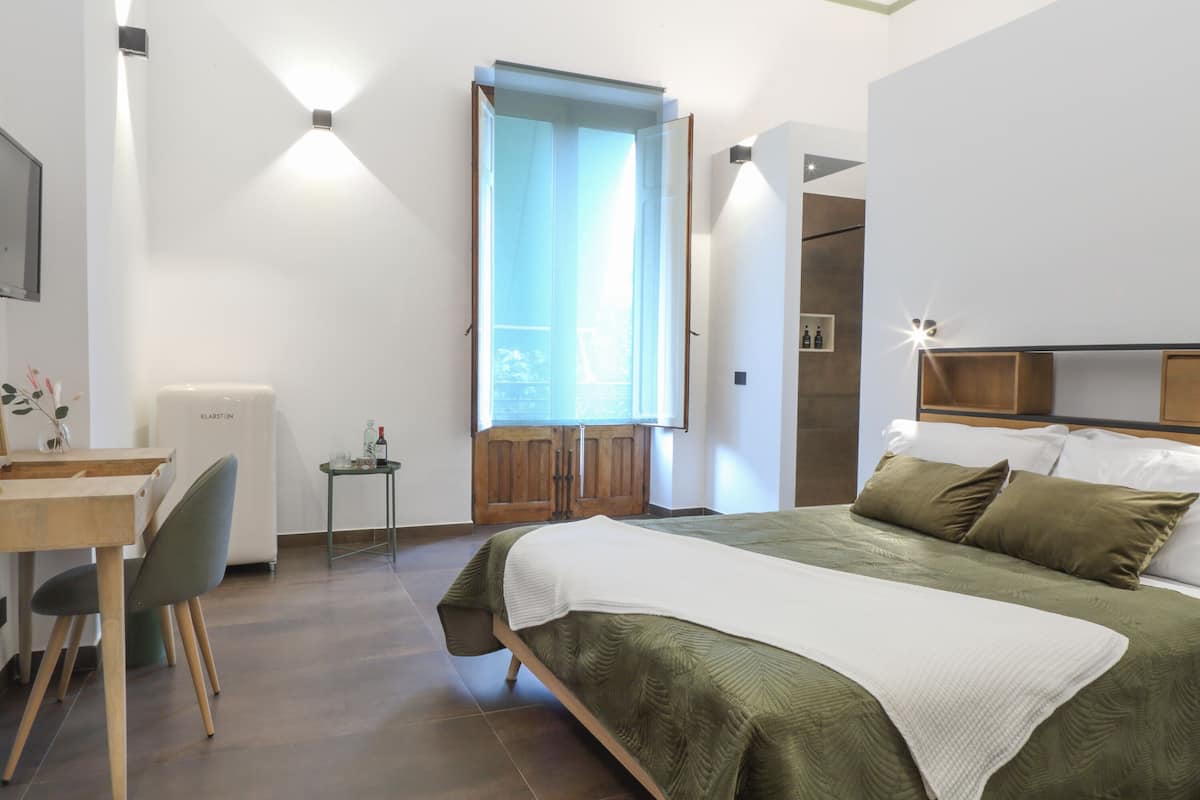 Un dormitorio con una cama, un escritorio, una silla, una mesita y una ventana con cortinas.