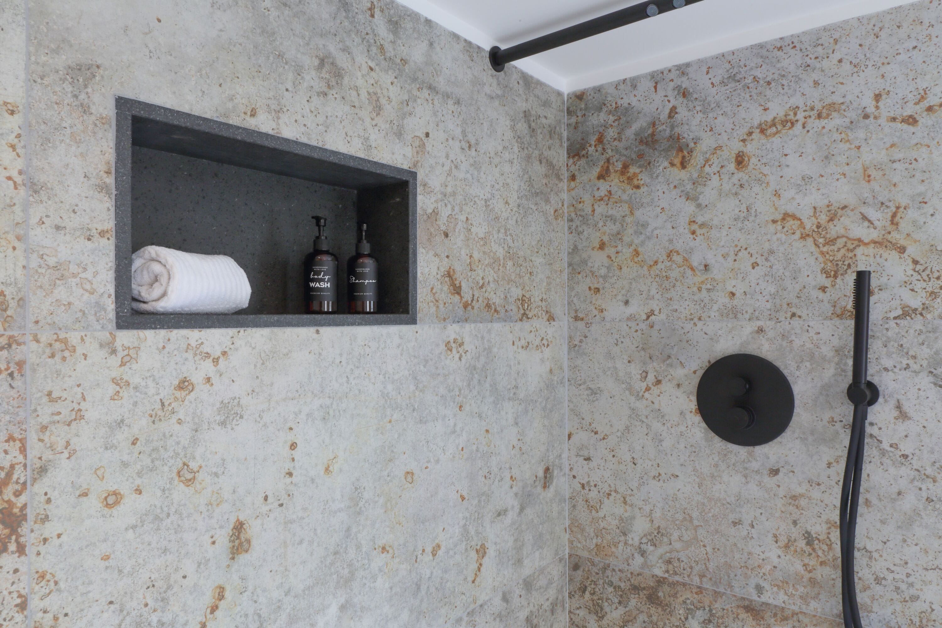 Un baño con pared de mármol, repisa con artículos de aseo y ducha.