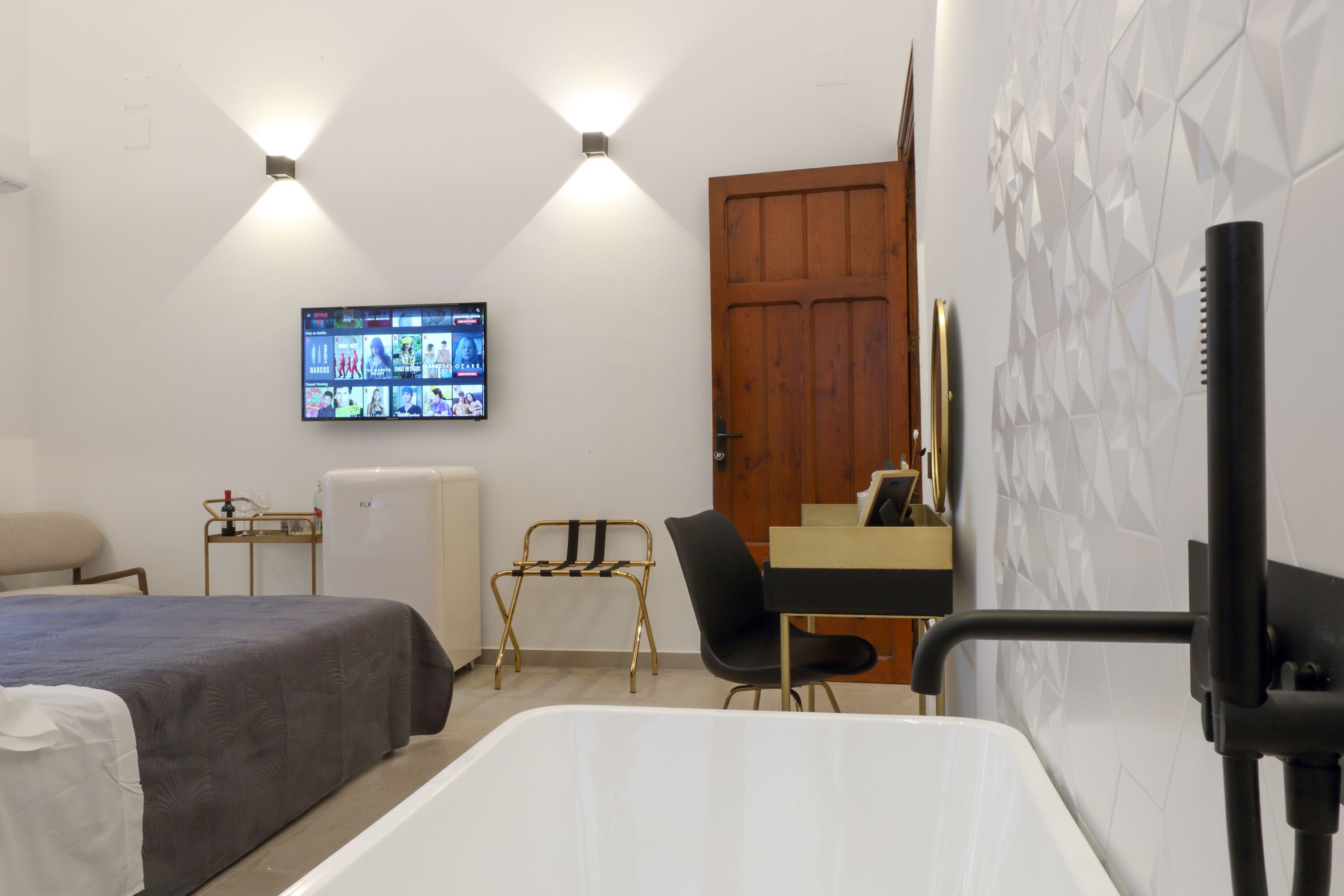 Habitación de hotel con cama, escritorio, silla, televisor montado en la pared y puerta de madera.