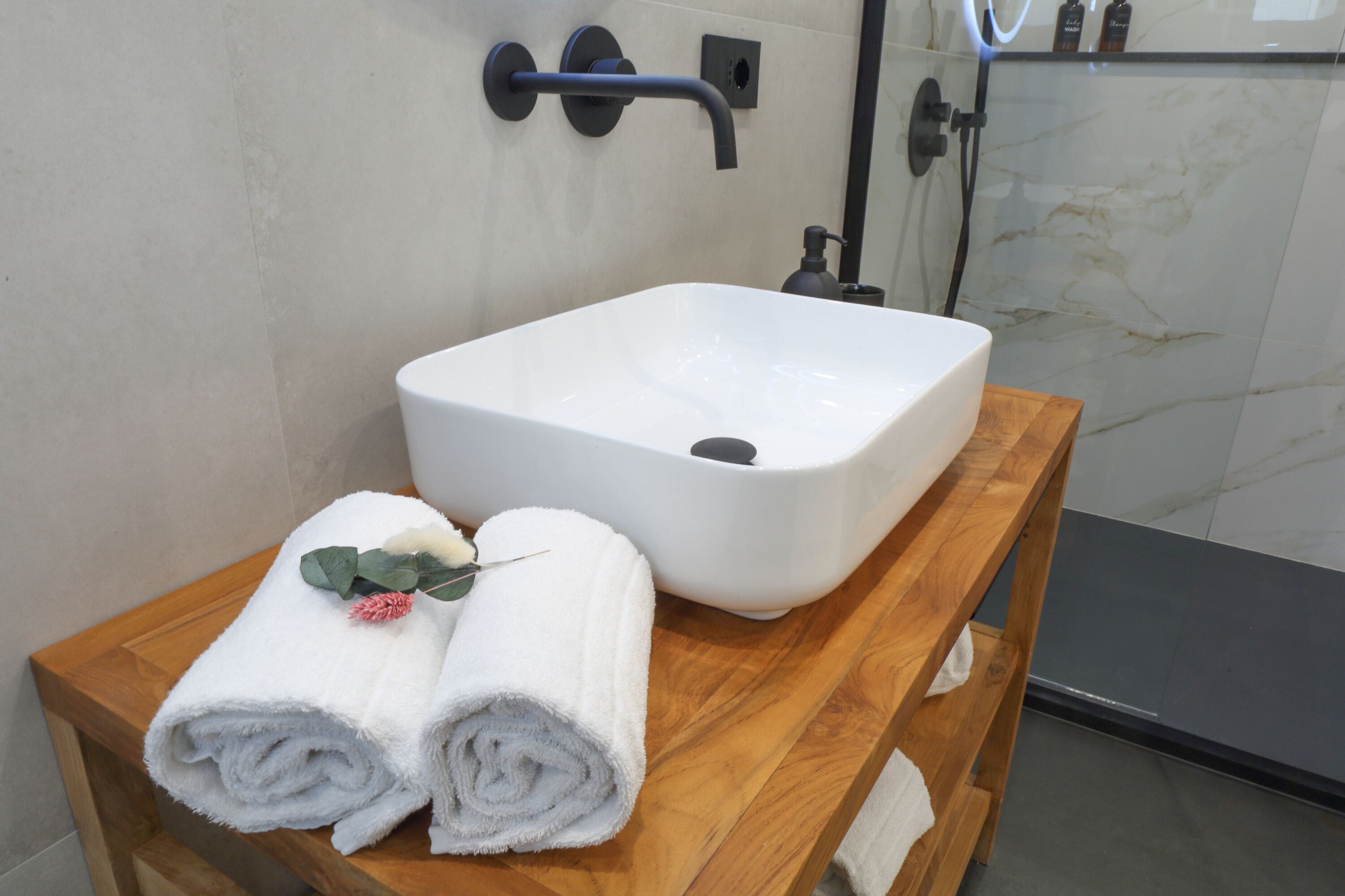 Une salle de bain avec un lavabo blanc, un meuble-lavabo en bois et un espace douche.