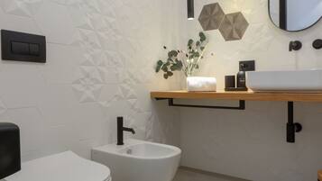 Un baño moderno con inodoro blanco, un bidé, un mueble de tocador de madera con lavabo y un espejo.