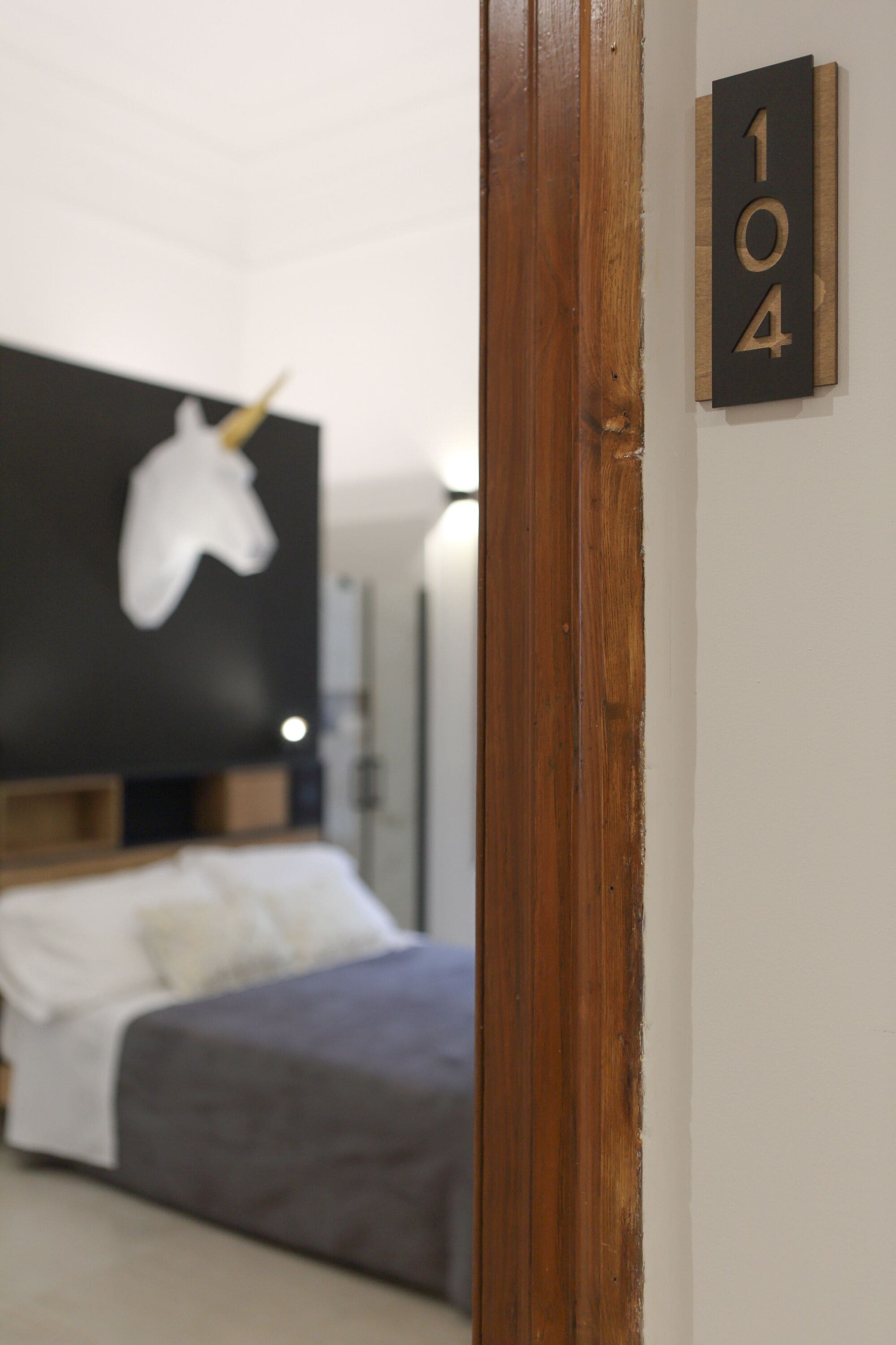Une chambre avec un lit, une porte en bois et un panneau indiquant le numéro de la chambre, fixé au mur.