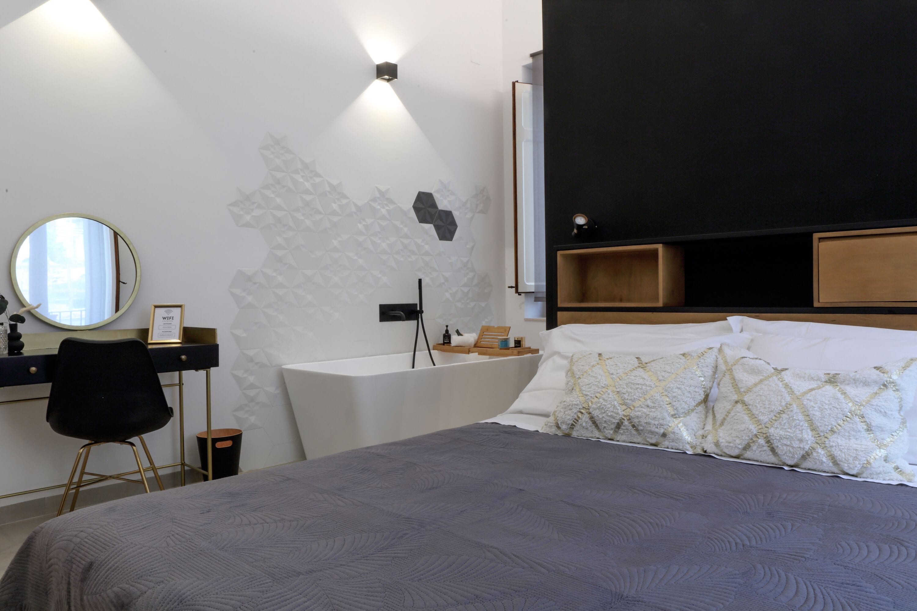 Une chambre d’hôtel moderne dotée d’un grand lit, d’un bureau avec une chaise, d’un miroir rond, d’une lampe fixée au mur et d’une étagère en bois.