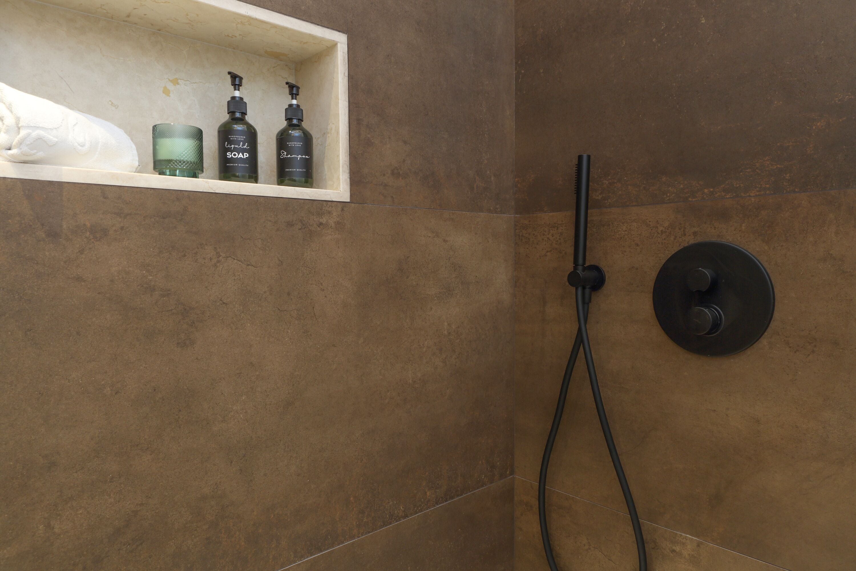 A shower area with a wall-mounted control panel and a shelf with toiletries.