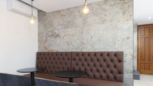 Un espacio de estar moderno con un sofá marrón capitonado, dos mesas redondas y dos sillas.