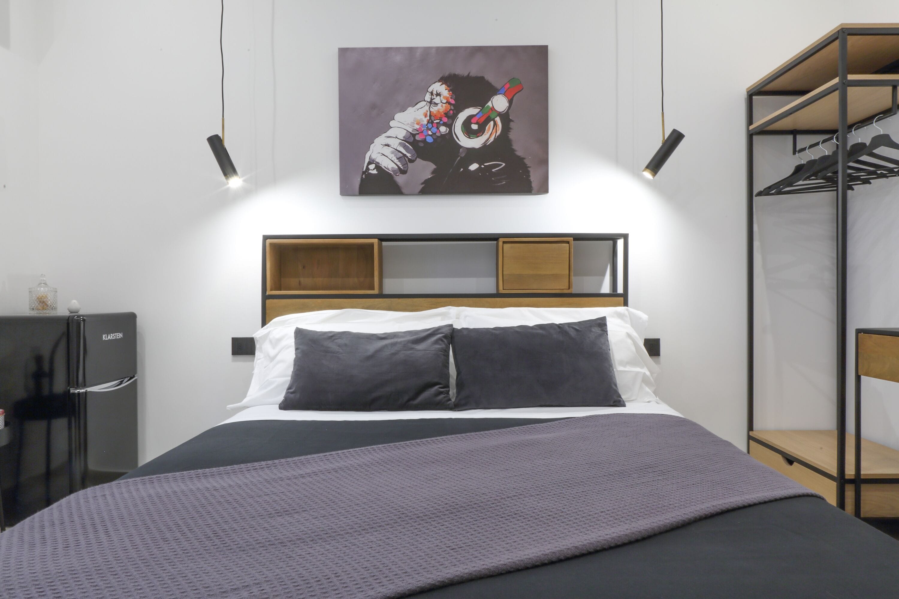 A modern hotel room with a bed, a wardrobe, and a painting on the wall.