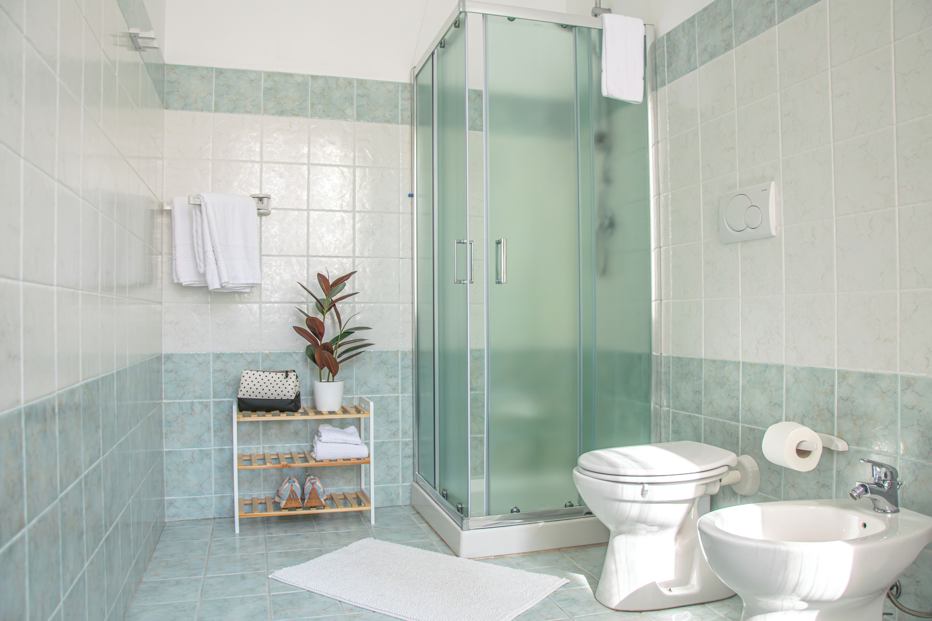 A bathroom with a glass-enclosed shower, a toilet, a sink, and a shelf with towels and toiletries.