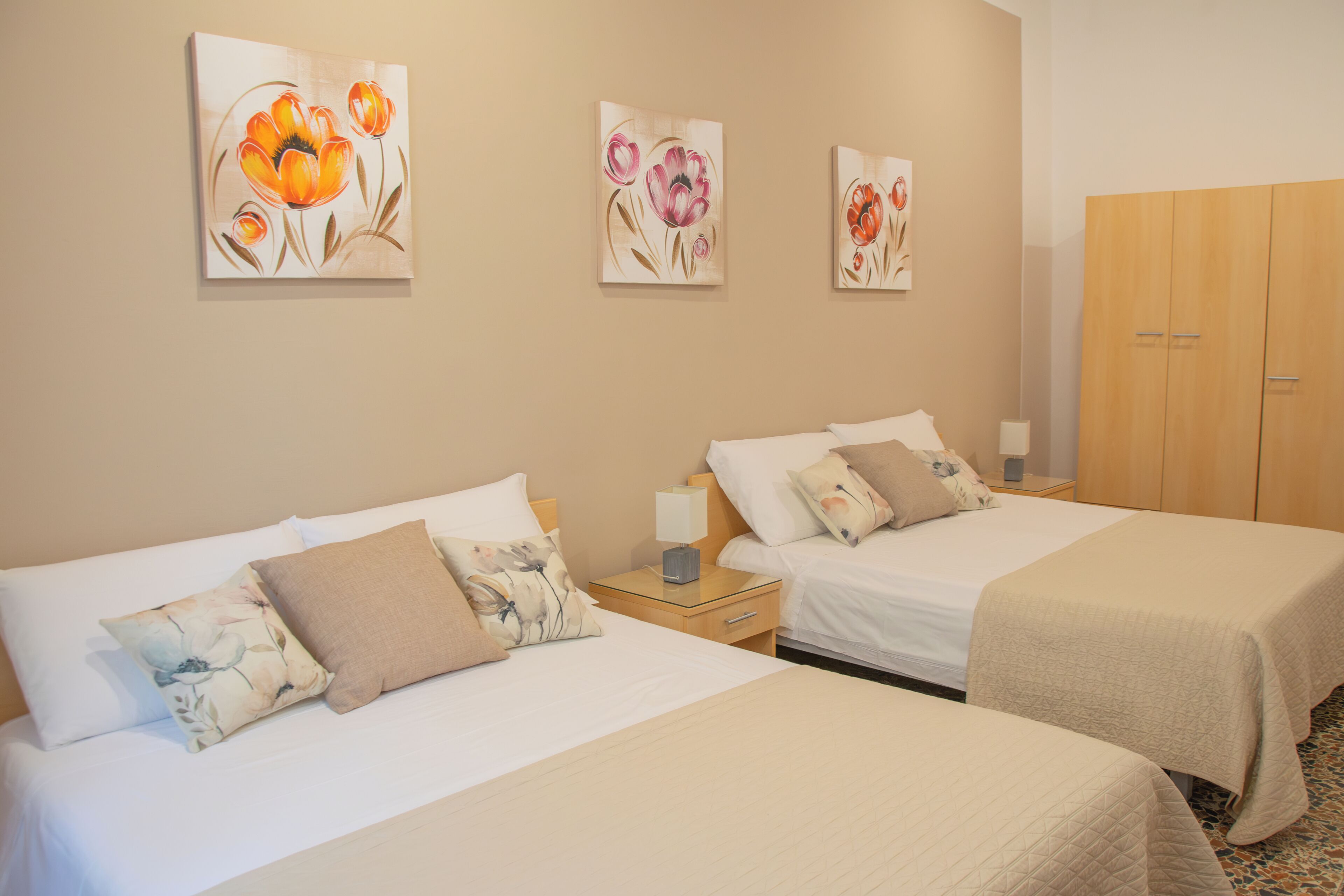 Ein Hotelzimmer mit zwei Betten, einem Kleiderschrank und drei floralen Bildern an der Wand.