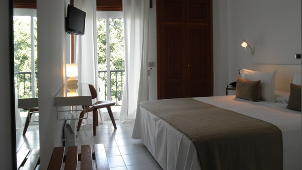 A hotel room with a bed, a desk with a chair, a television mounted on the wall, and a large window with curtains. - Farsund (Sanxenxo)