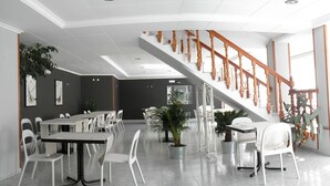 A spacious dining area with multiple tables and chairs, a staircase with wooden railings, and potted plants. - Farsund (Sanxenxo)