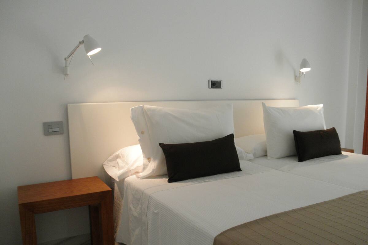 A hotel room with a bed, two bedside tables, and two wall-mounted lamps.