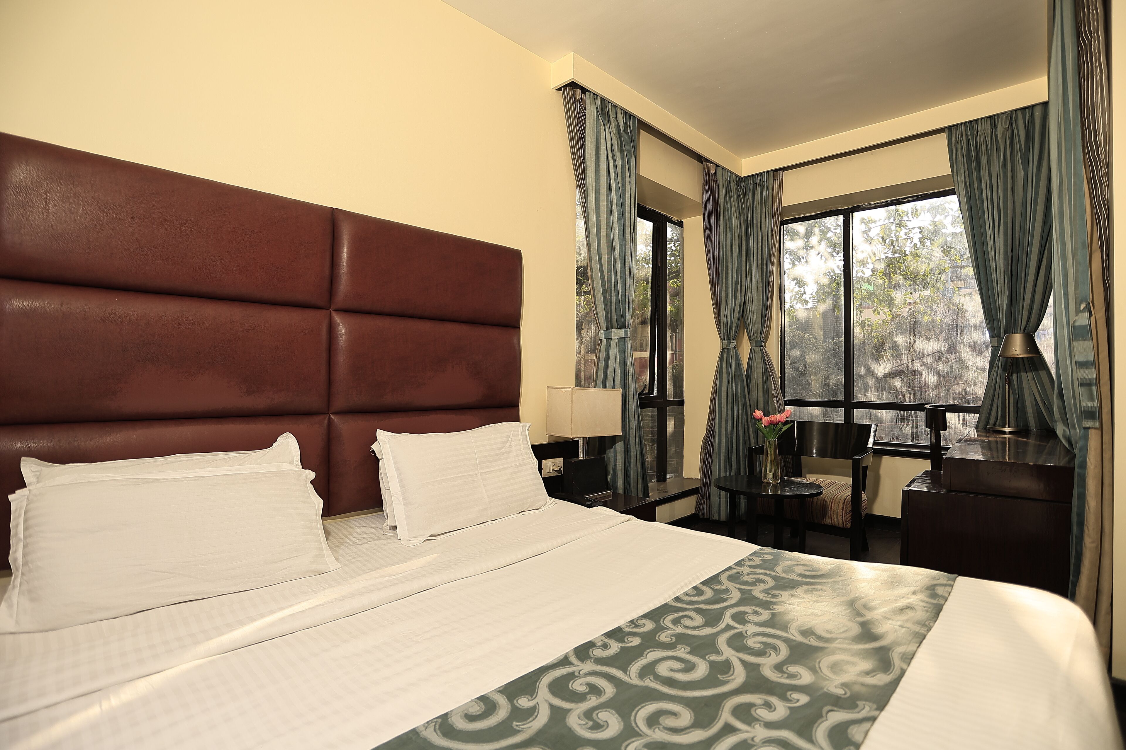 Una habitación de hotel con una cama grande, cabecera, escritorio, silla, lámpara y cortinas.