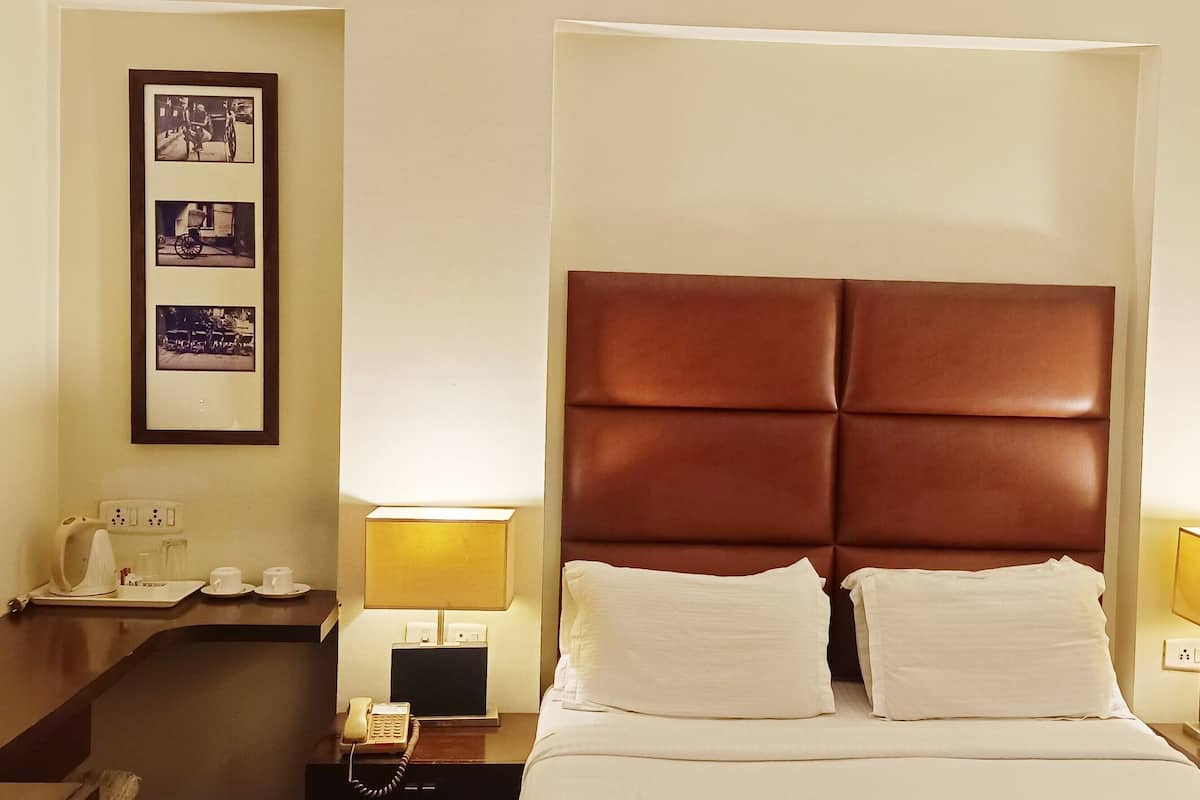 Habitación de hotel con una cama grande, dos lámparas de noche, una mesita de noche con teléfono y un marco de fotos colgado en la pared.