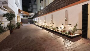 Un estrecho callejón con macetas a lo largo de las paredes, una cerca de madera y la entrada de un edificio con un letrero.