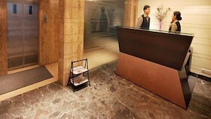 Un área de recepción con piso de mármol, un mostrador de recepción y un espejo que refleja a dos personas.