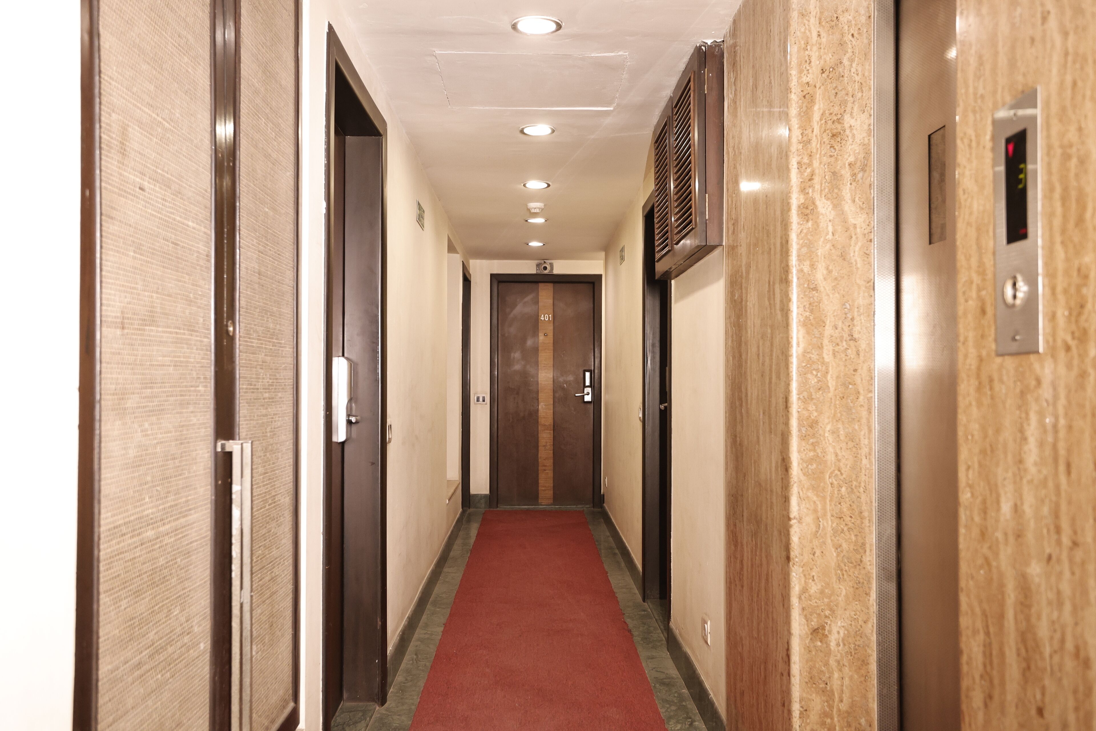 A hotel hallway with a red carpet, wooden doors, and an elevator.