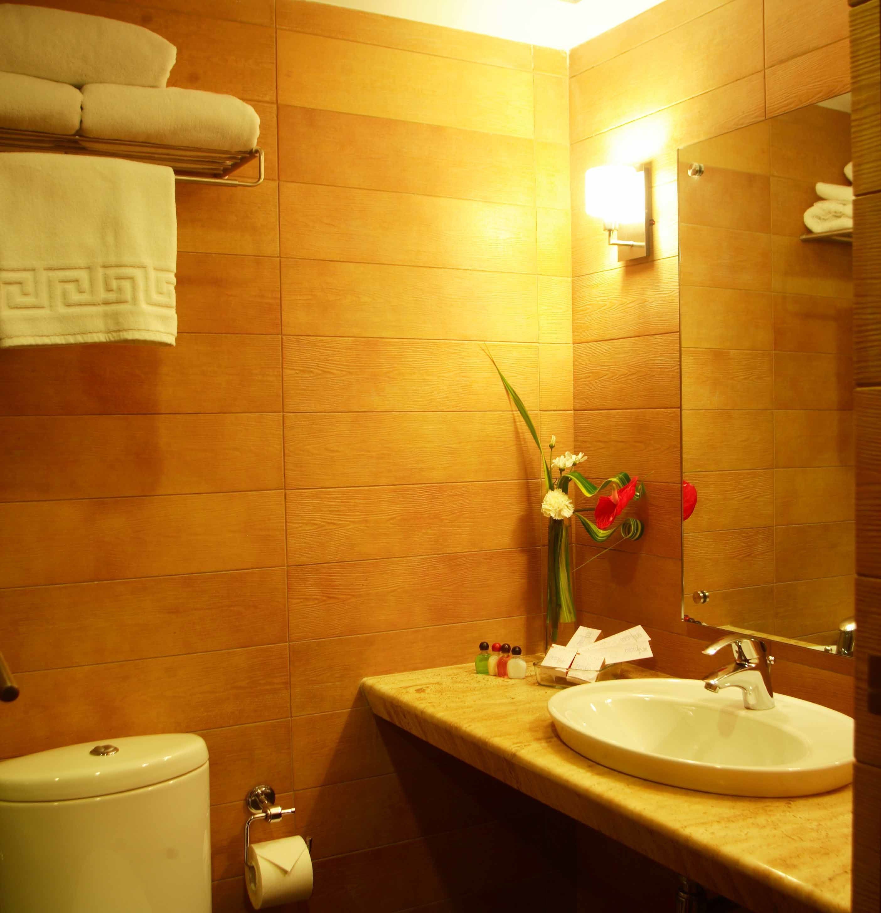 Une salle de bain avec des murs en bois, des toilettes, un lavabo et un miroir. Des serviettes sont accrochées au mur et un vase rempli de fleurs est posé sur le comptoir.