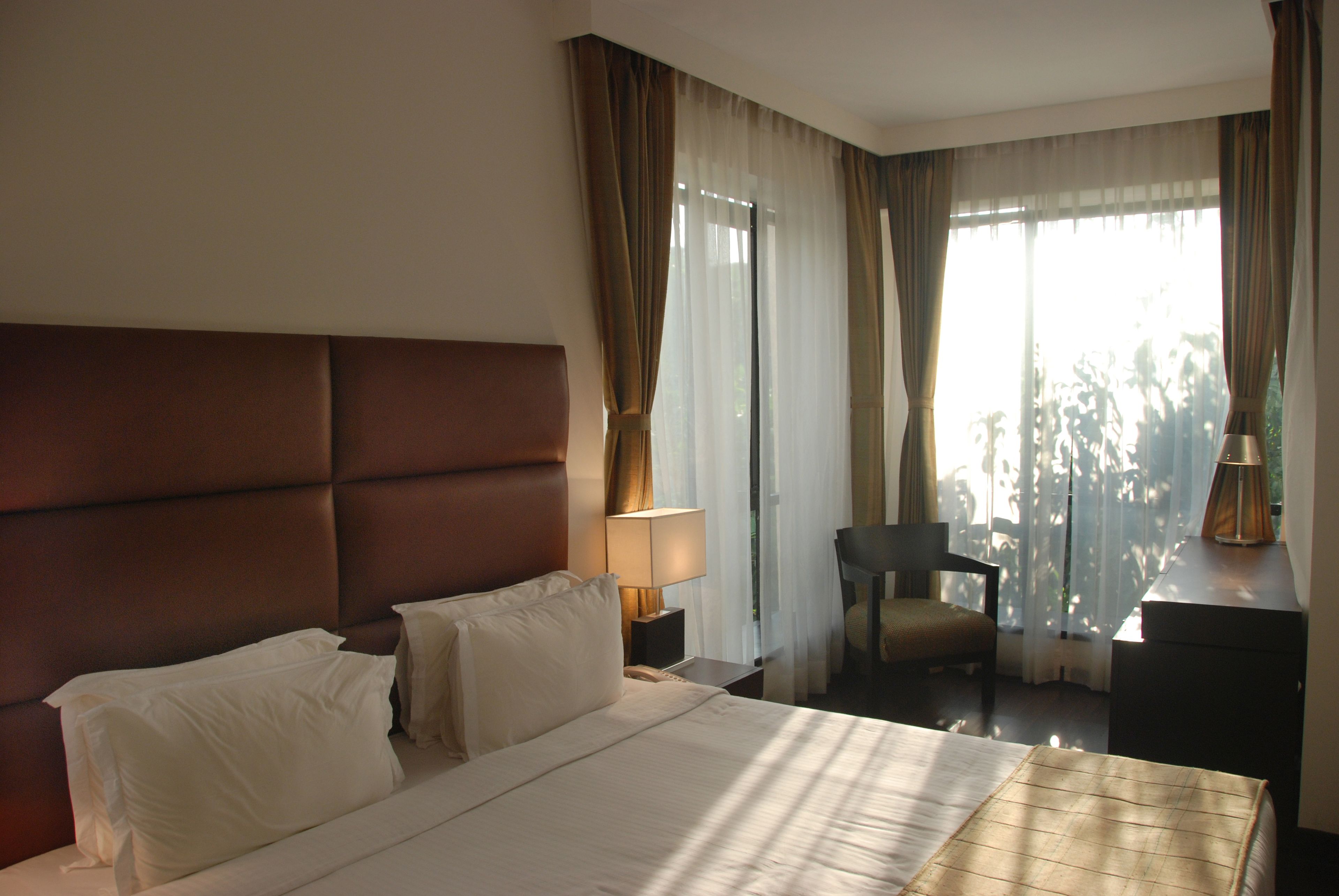 A hotel room with a large bed, a nightstand, a chair, and a desk with a lamp.