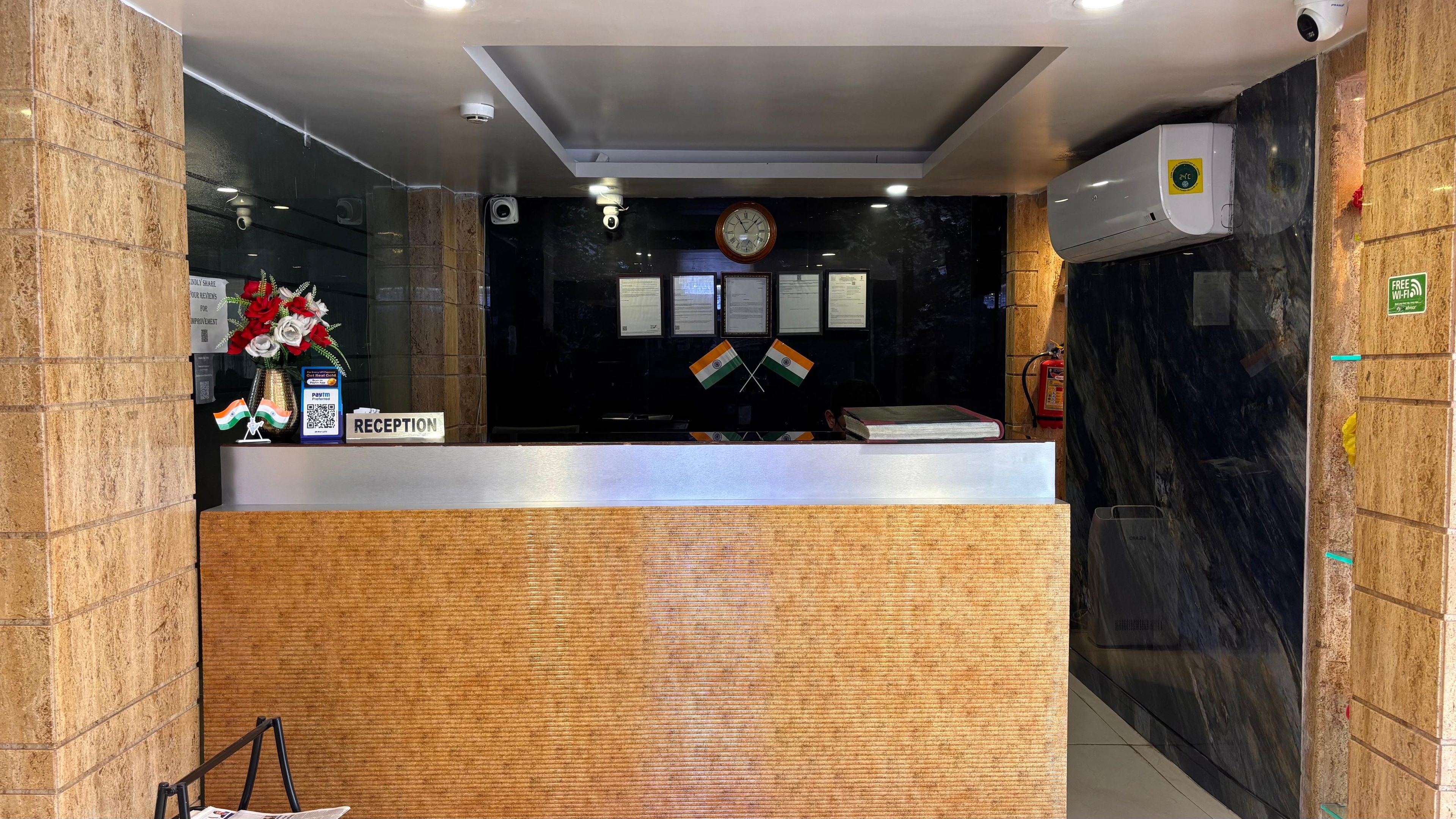 Un comptoir d’accueil surmonté d’une horloge, des certificats encadrés accrochés au mur et deux drapeaux indiens.