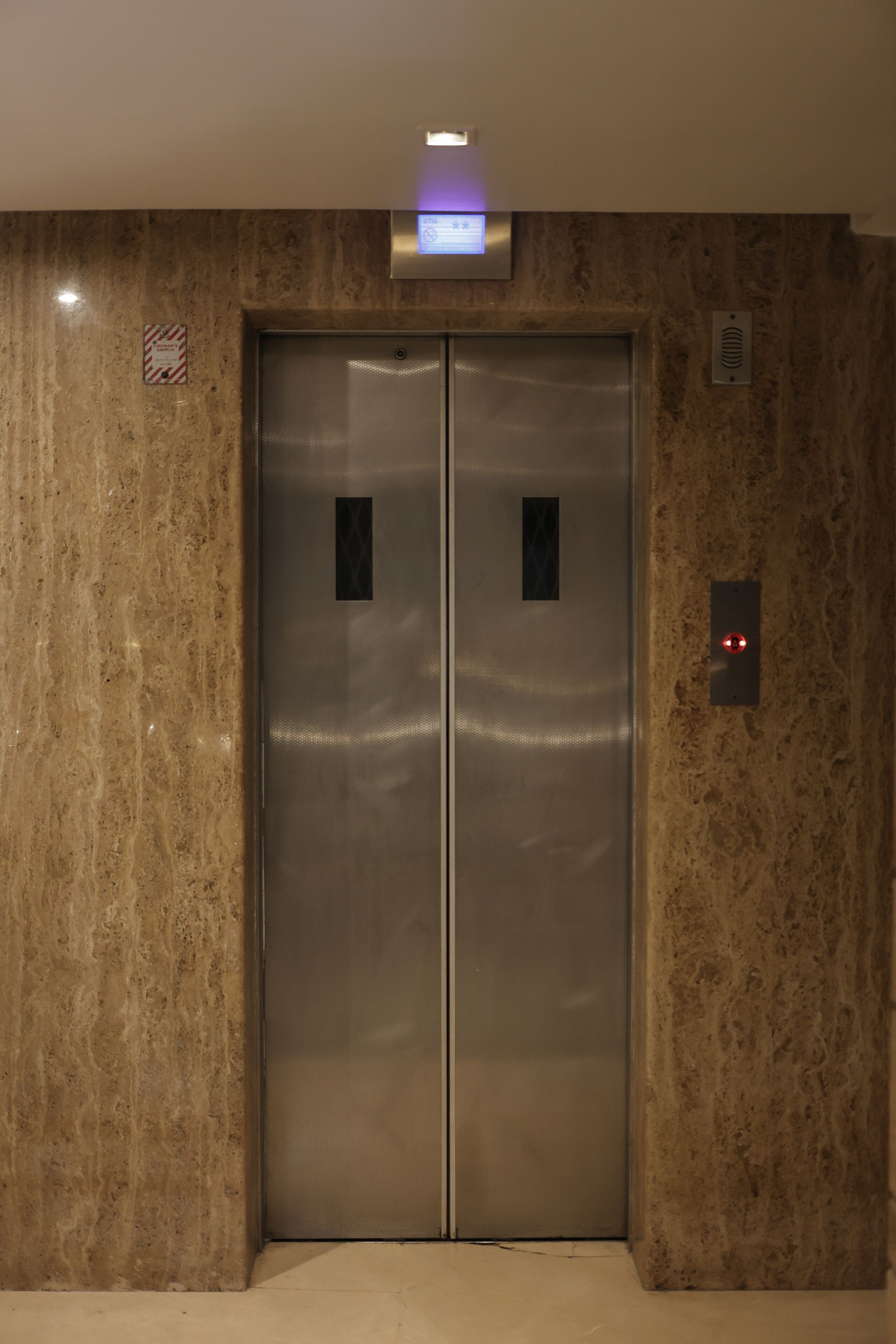 A modern elevator with a metallic finish, set in a room with marble walls.
