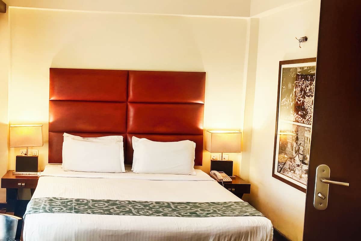 Habitación de hotel con una cama grande, dos mesitas de noche, una silla y una puerta con picaporte.