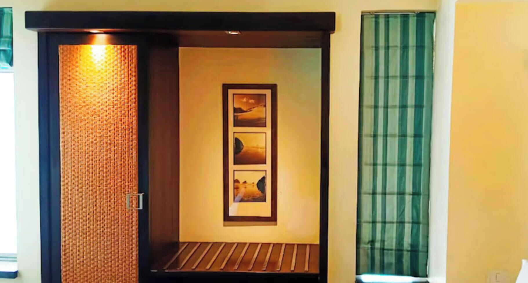 Une pièce avec un mur à texture, un tableau encadré, un banc et une fenêtre ornée de rideaux verts.