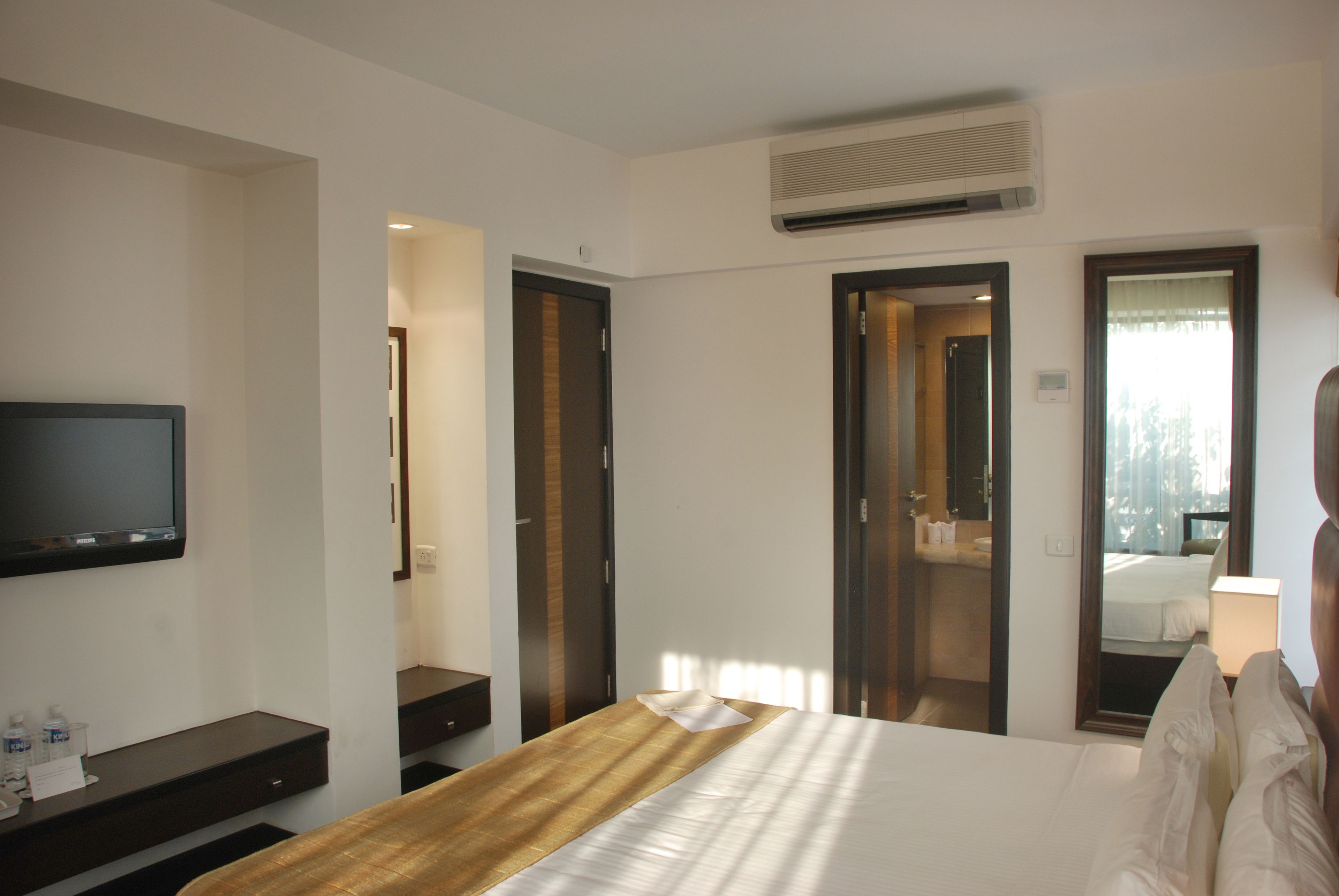 A hotel room with a bed, a TV, a desk, and a bathroom visible through an open door.