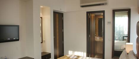A hotel room with a bed, a TV, a desk, and a bathroom visible through an open door.