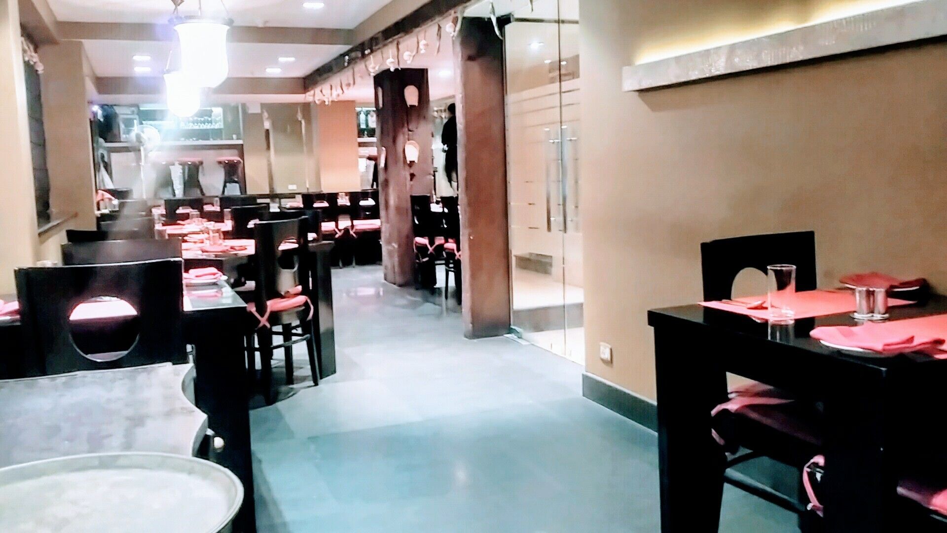A restaurant with multiple tables and chairs, a central aisle, and a modern interior design.