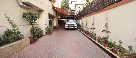 Un estrecho callejón con un coche aparcado, plantas en macetas y la entrada de un edificio.