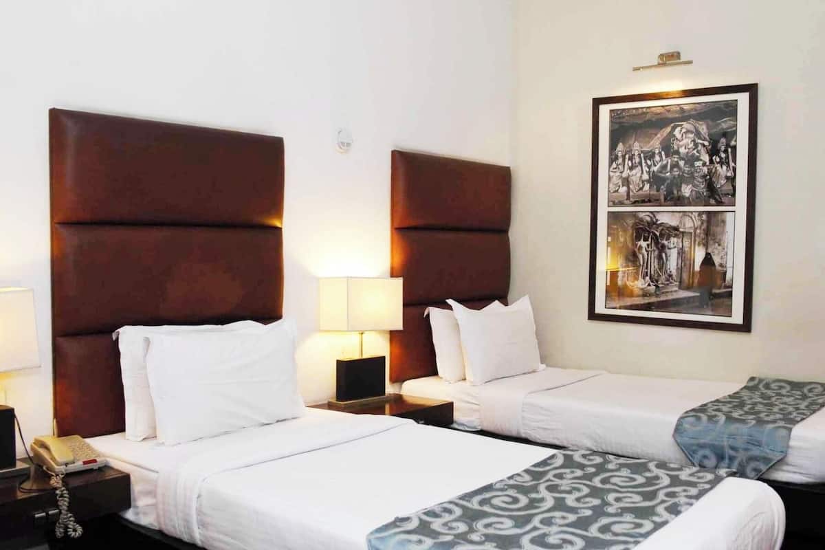 Una habitación de hotel con dos camas, cada una con cabecero, mesitas de noche con lámparas y un cuadro en la pared.