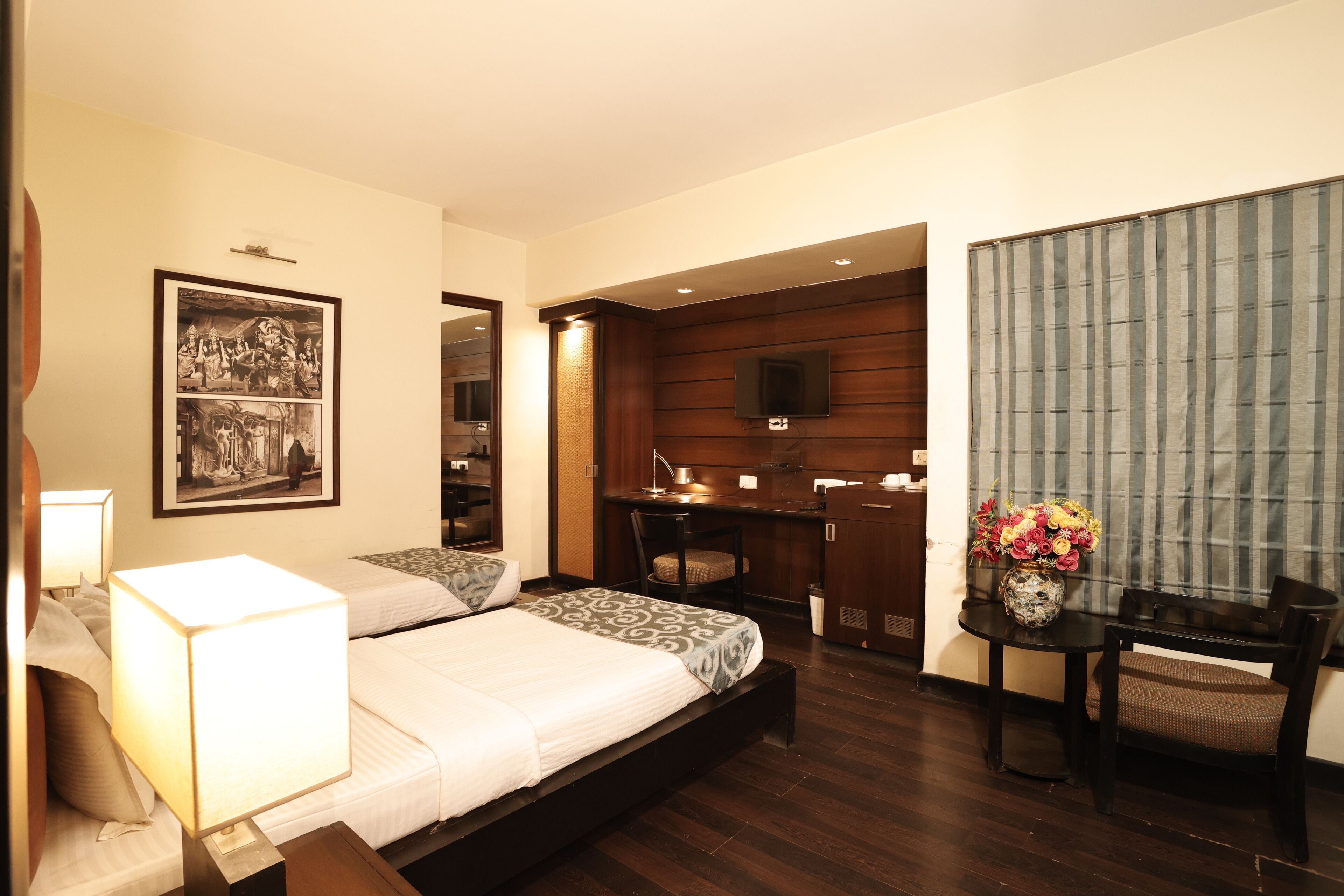 A hotel room with a bed, bedside table, lamp, desk, chair, TV, and a framed picture on the wall.