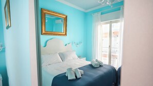 Habitación de hotel con una cama grande, un espejo con marco dorado y vista al balcón exterior.