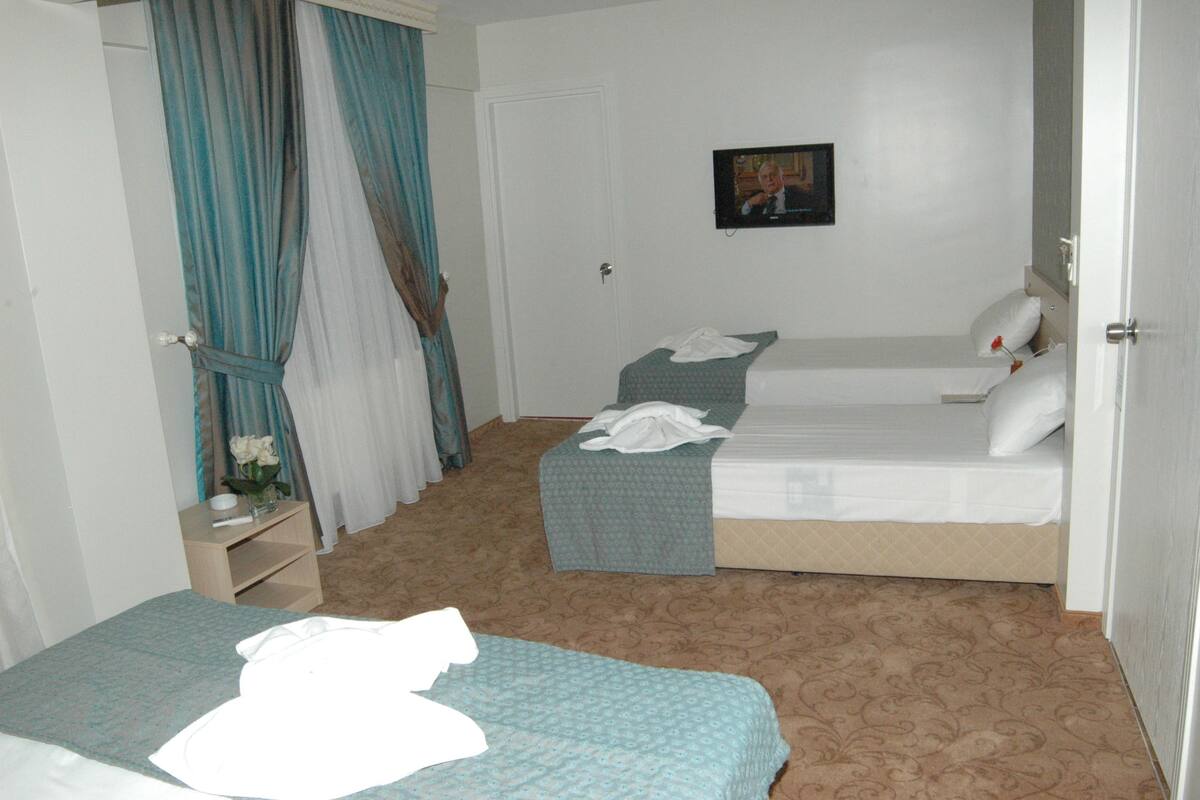 A hotel room with two beds, a small bedside table, a TV on the wall, and a door.
