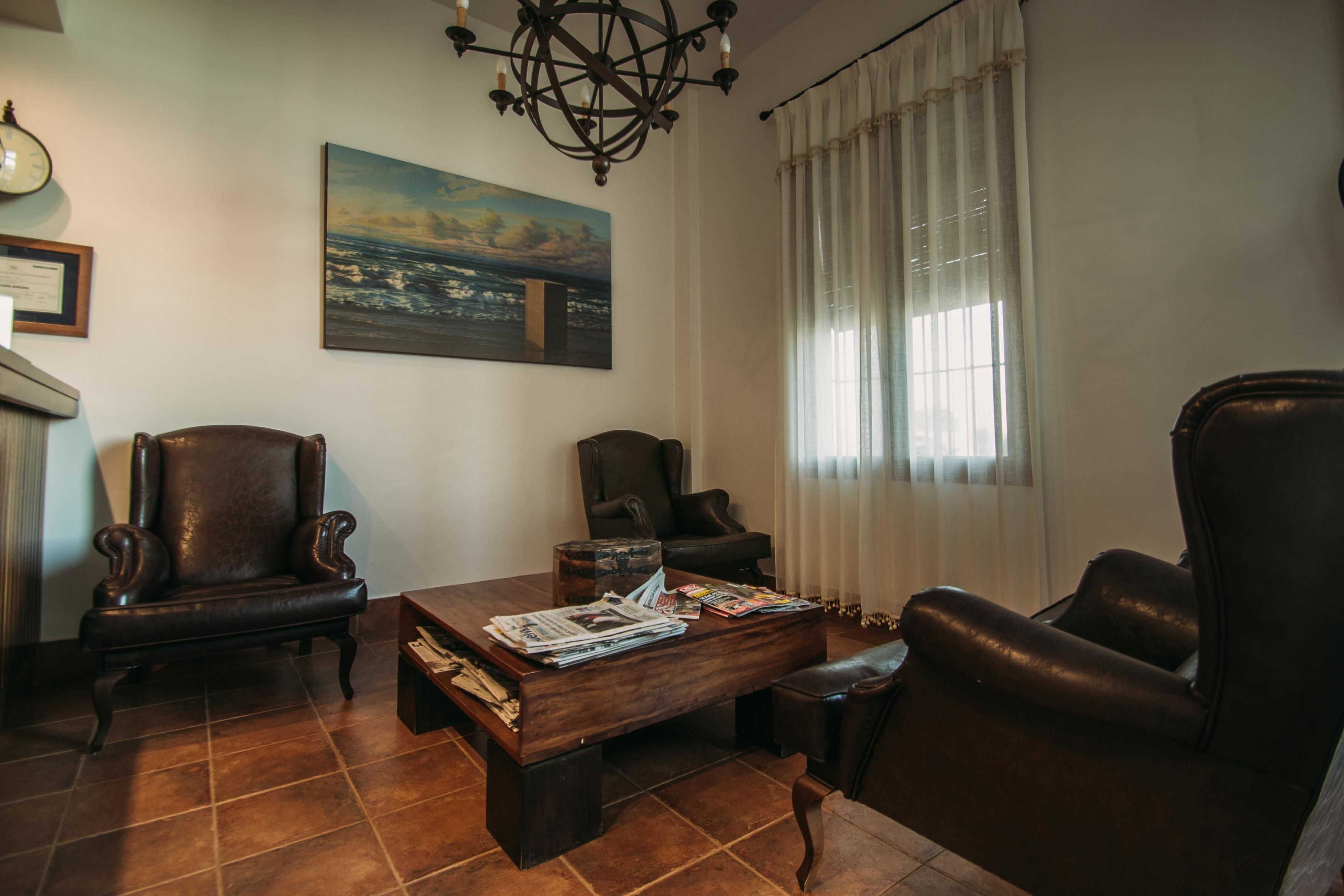 Una sala de estar con una mesa de centro de madera, dos sillones de cuero, un cuadro grande y una araña.