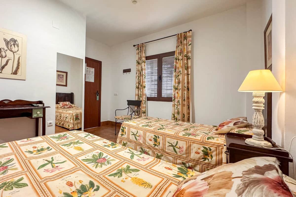 Ett hotellrum med två sängar, ett skrivbord, en stol, en lampa och ett fönster med gardiner.