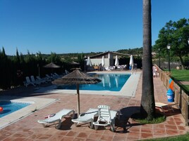 Una piscina con sillas de descanso y sombrillas, una valla de madera y un edificio al fondo.