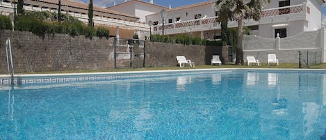 Una piscina al aire libre, sombrillas, sillones reclinables de piscina