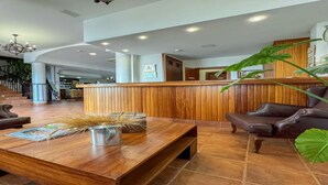 A spacious lobby with a wooden reception desk, leather armchairs, and a coffee table with magazines and decorative items. - Hotel Valsequillo (Lepe)