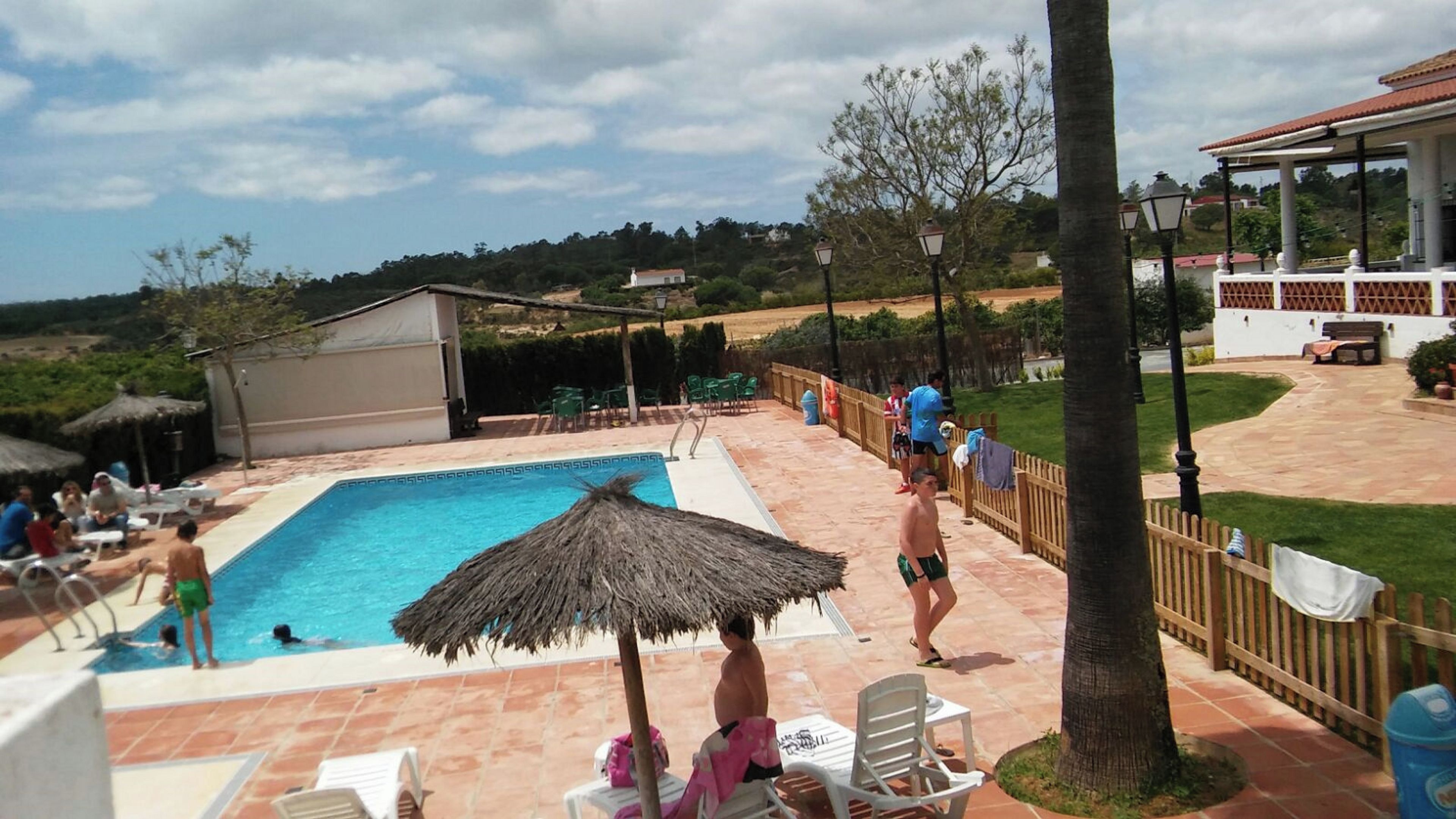 Una piscina con sombrilla de paja, rodeada de sillas de descanso y una cerca de madera.