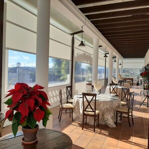 An outdoor dining area with tables and chairs, large windows, and a view of the cityscape.