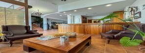 A spacious lobby with a wooden reception desk, leather armchairs, and a coffee table with magazines and decorative items.