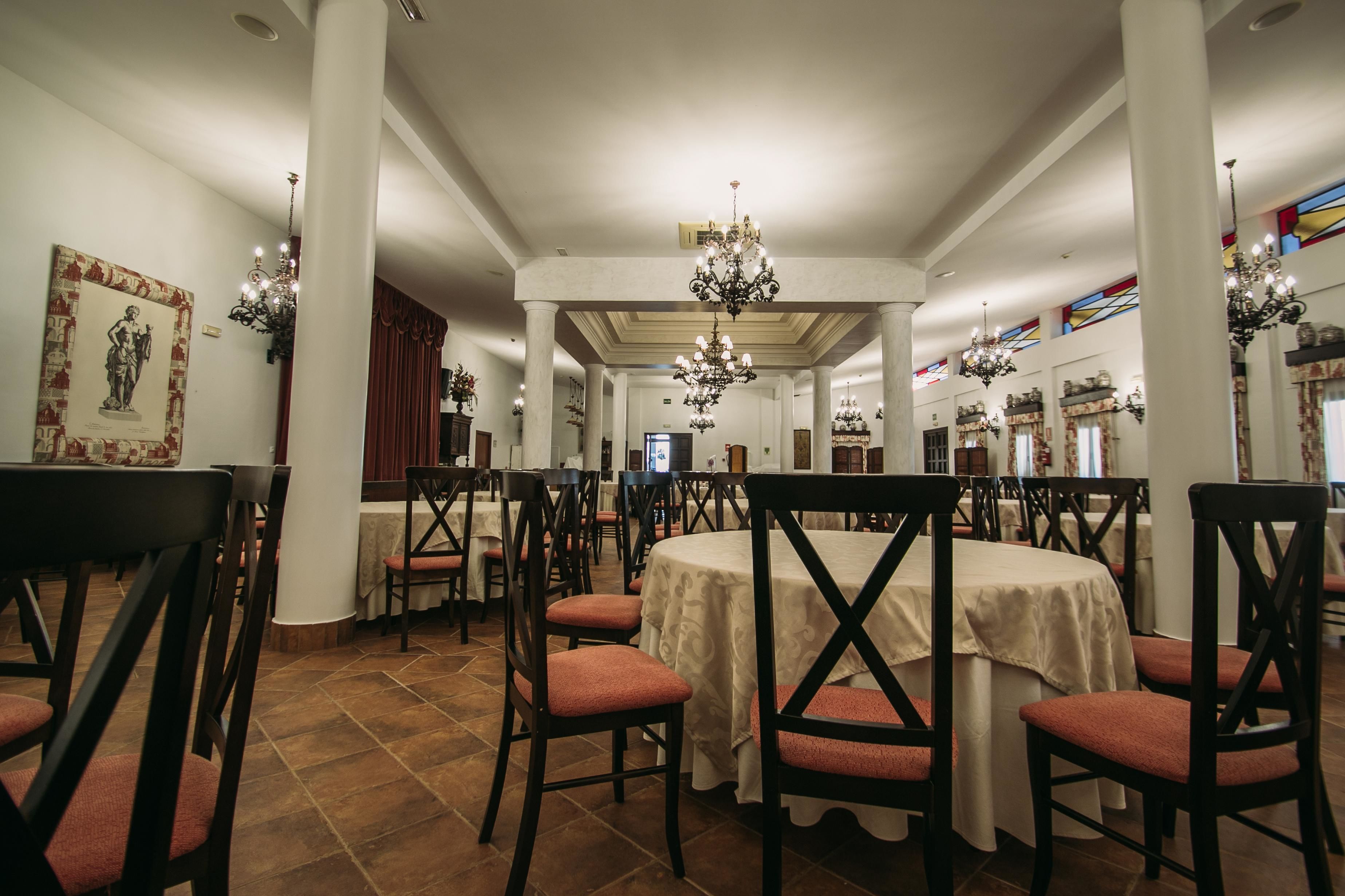 Un comedor con mesas redondas, sillas tapizadas en rojo y candelabros.