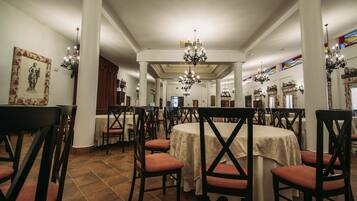 Un comedor con mesas redondas, sillas tapizadas en rojo y candelabros.